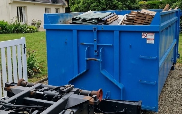 Benne ampliroll 12 m³ bleue chargée, posée devant une maison