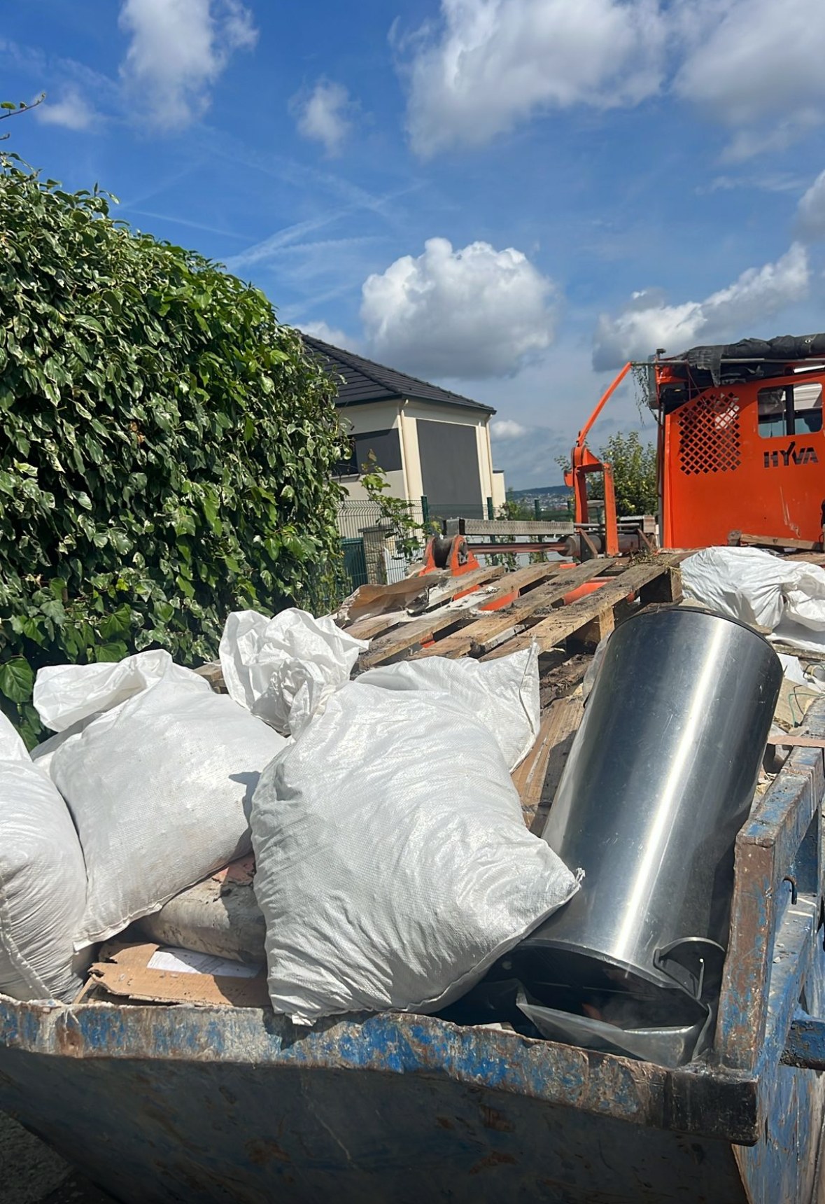 Benne posée devant une maison, chargée de sacs de gravats